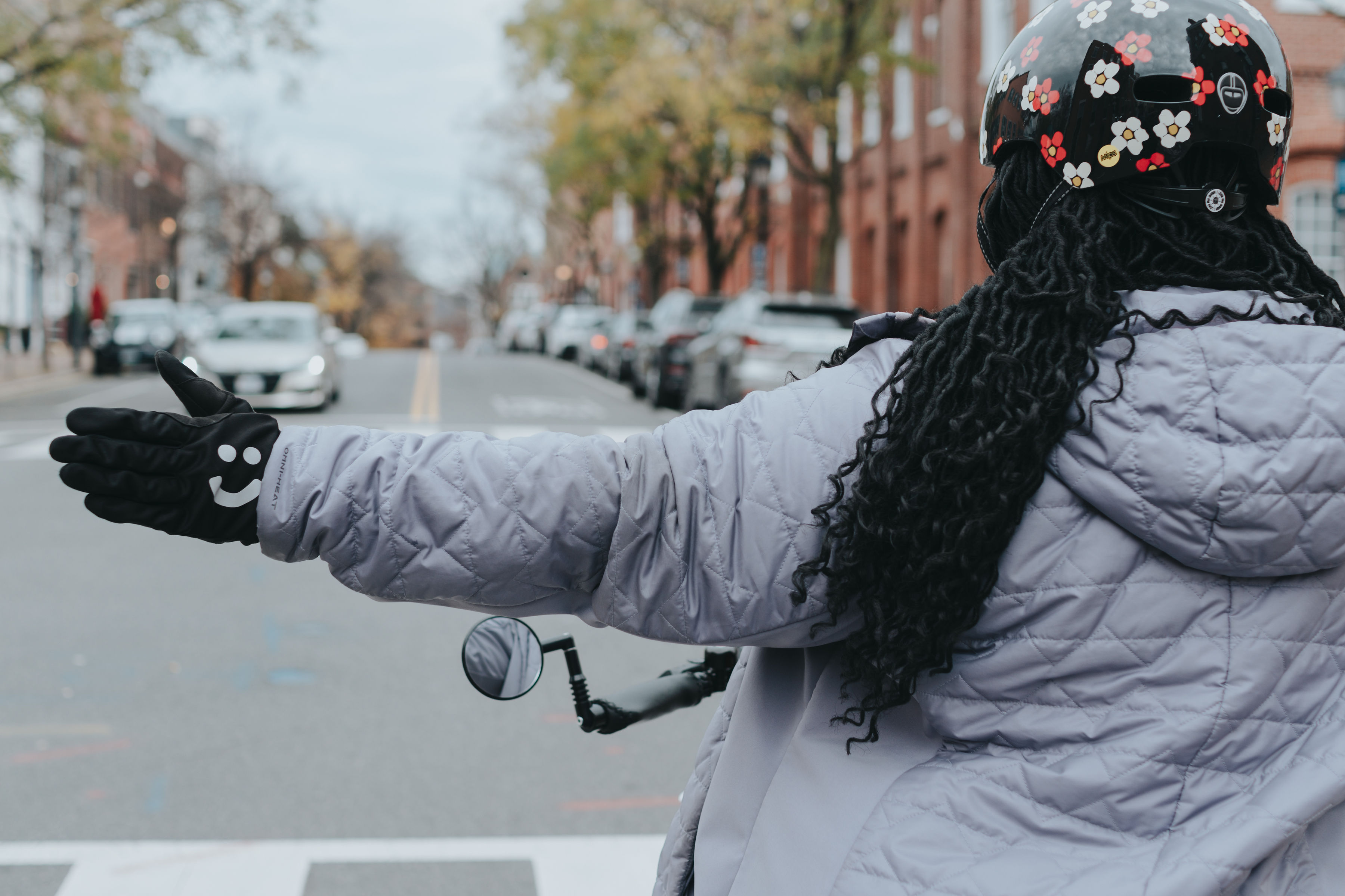 Closeup photo of person riding on bicycle in Old Town signaling a turn. They have a smiley face on the hand they're using to signal :)