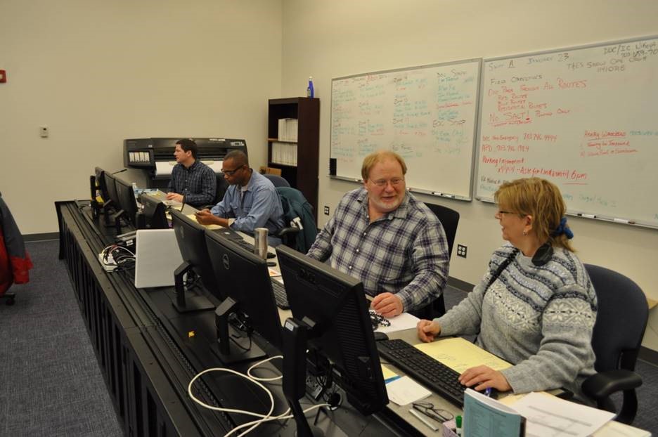 Four people sit at a long desk filled with computer monitors in the traffic center