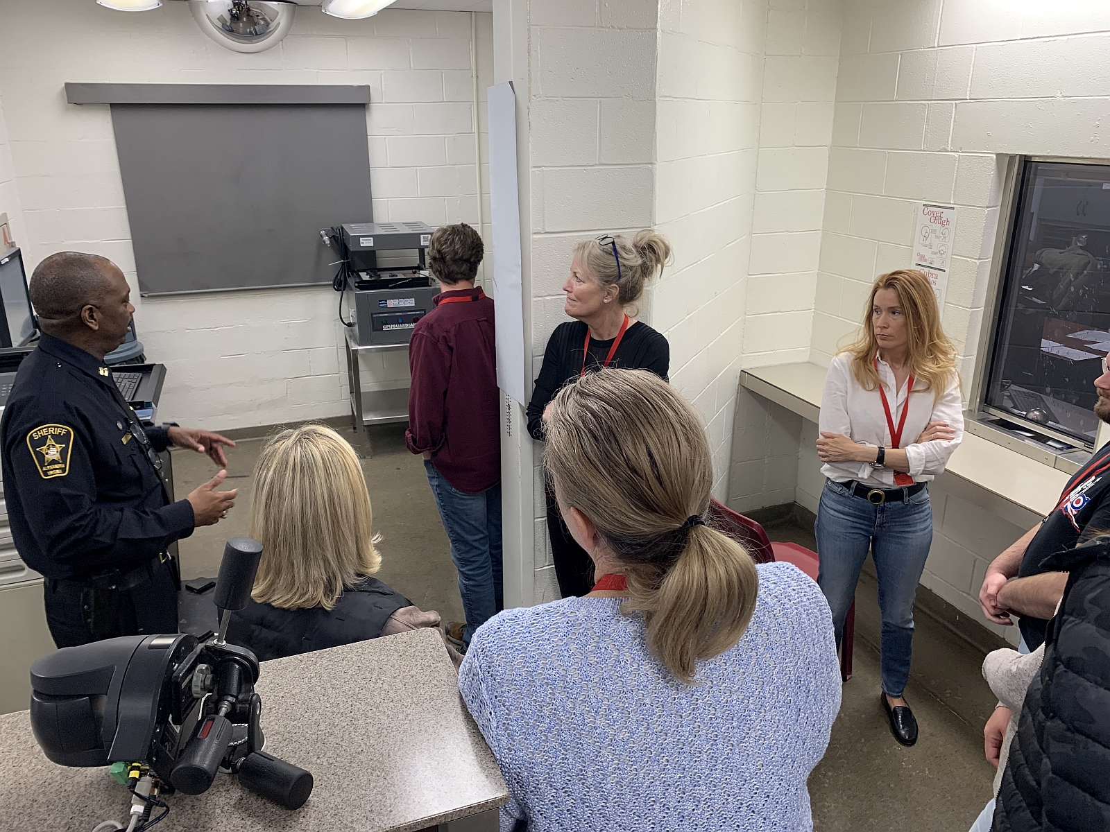 Uniformed Sheriff's Office commander speaking to six civilians inside the booking area of the jail