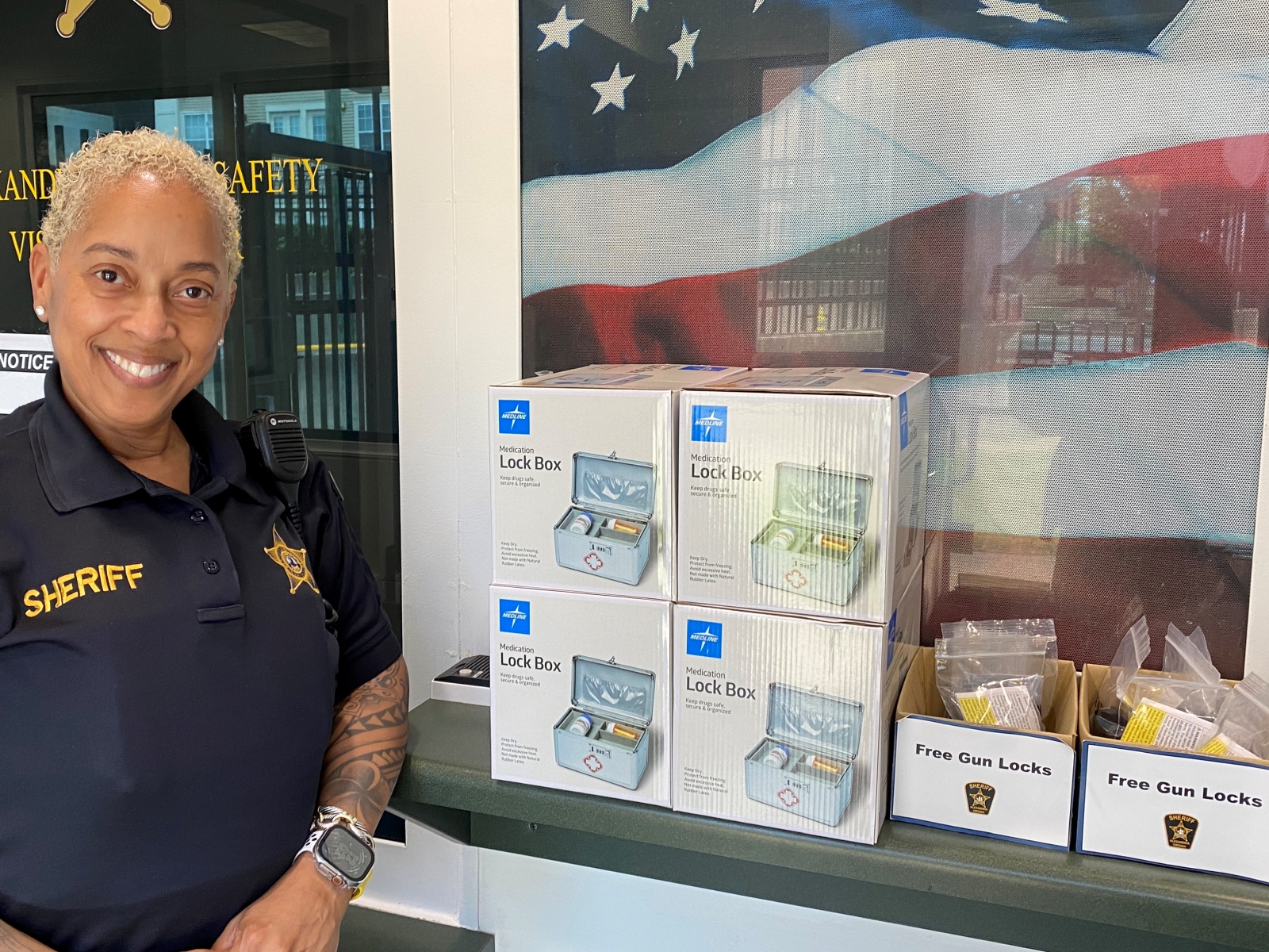 deputy standing next to display of small lock boxes in cartons and smaller boxes with labels reading Free Gun Locks