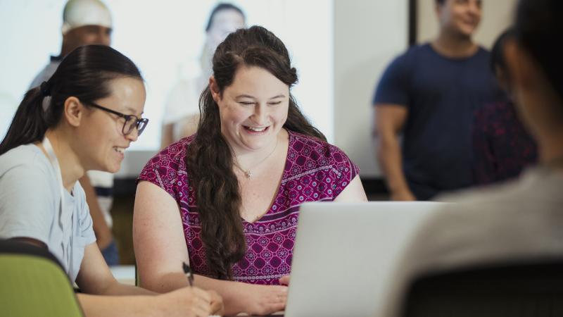 Adults learning together at a table with a laptop.