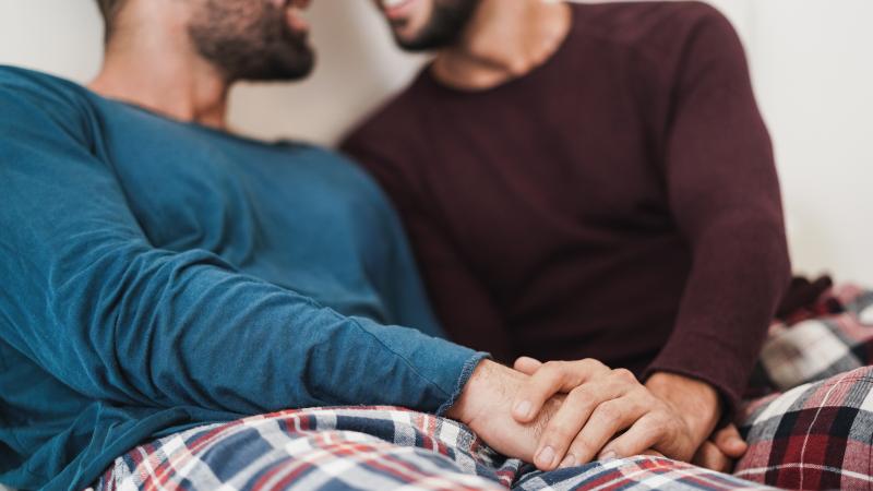 two smiling bearded men hold hands and sit facing each other