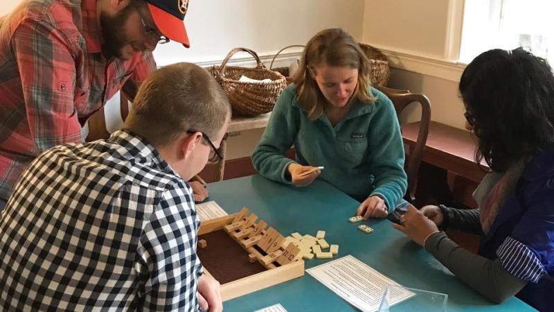 Four people gathered around table playing historic games.