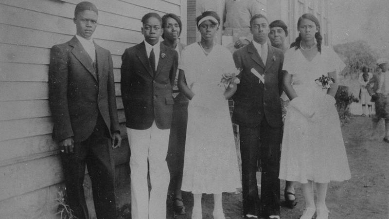 A few students in front of wooden schoolhouse