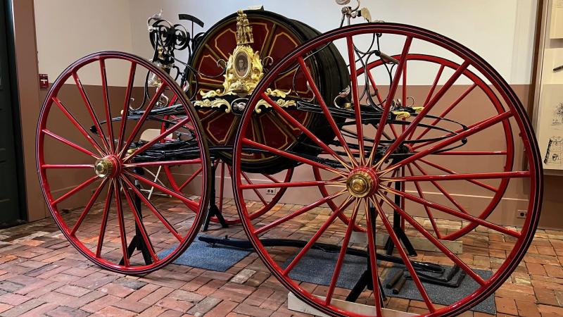 Historic fire pumper with four large thin wheels and a red body. 