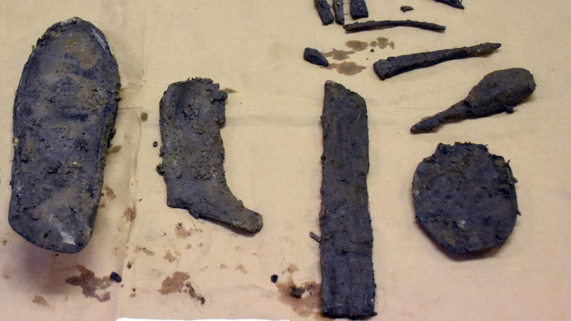 Pieces of leather shoes are laid out on brown paper to be photographed with a scale.