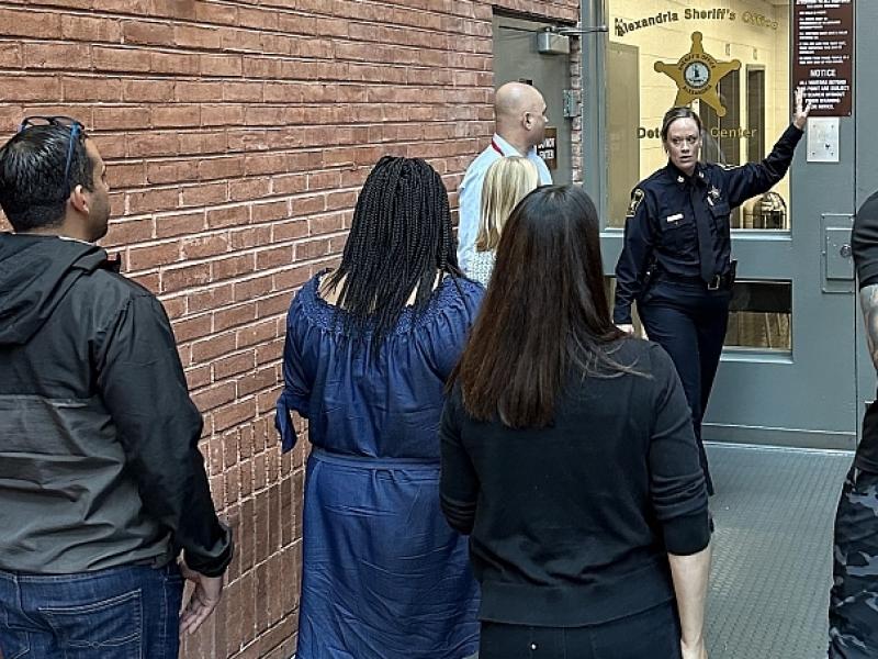 Sheriff's Office commander in blue uniform giving tour to seven community members entering the jail