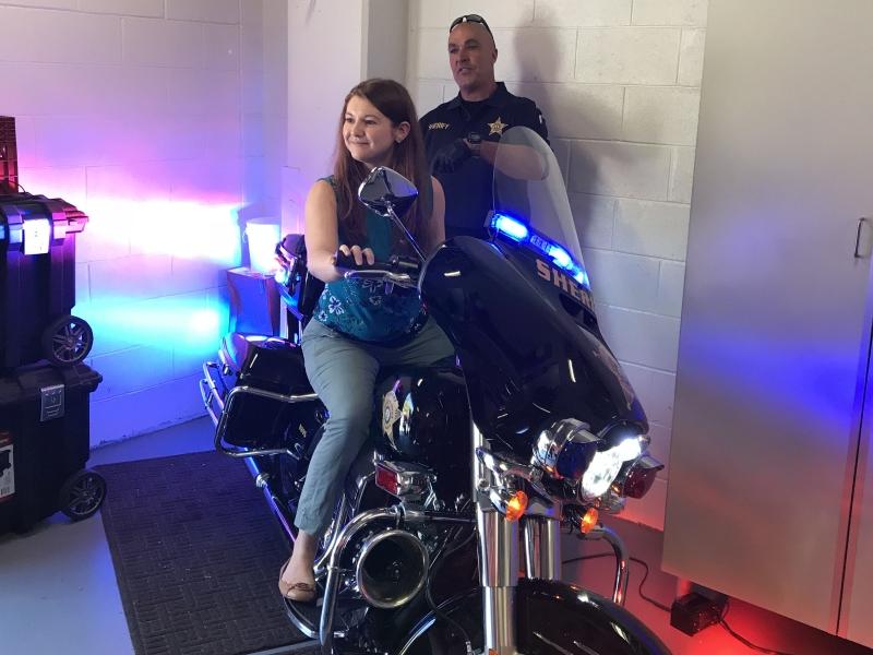 civilian sitting on a Sheriff's motorcycle with deputy in background