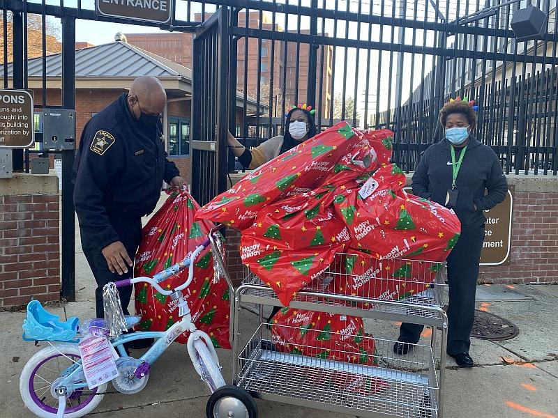 deputy and two civilians with child's bicycle and large holiday gift bags