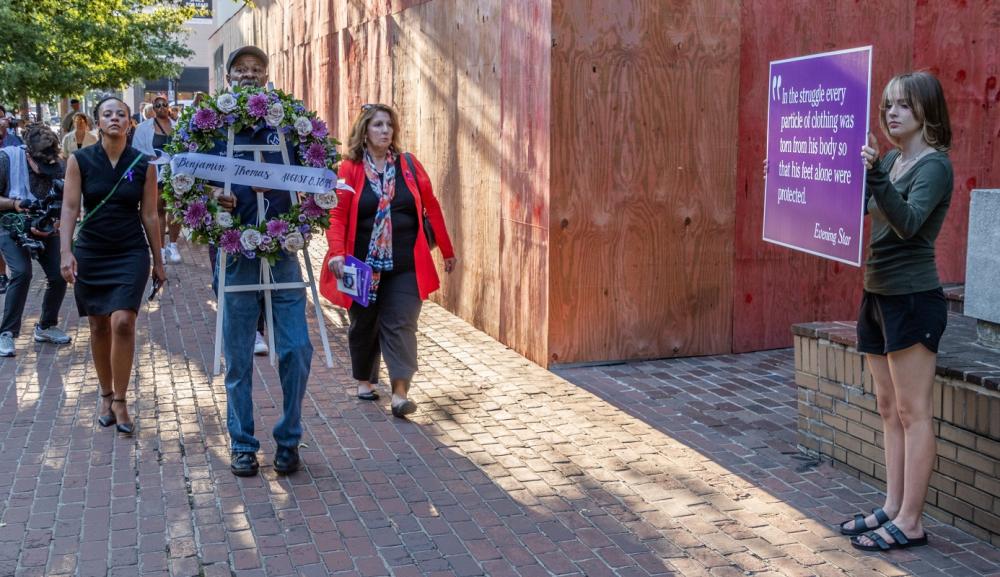 The procession passes by a student holding a sign