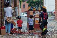 A child uses a hose to “extinguish” pretend flames painted on a miniature plywood house.