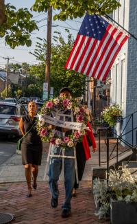 Procession with wreath passing house with flag.