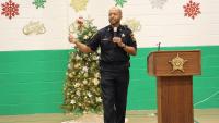 deputy in a blue information holding a microphone and speaking with a Christmas tree and decorations in the background