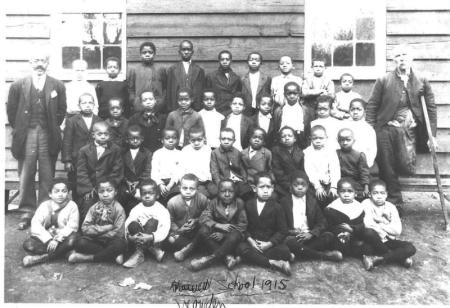 teachers and children in front of wooden building