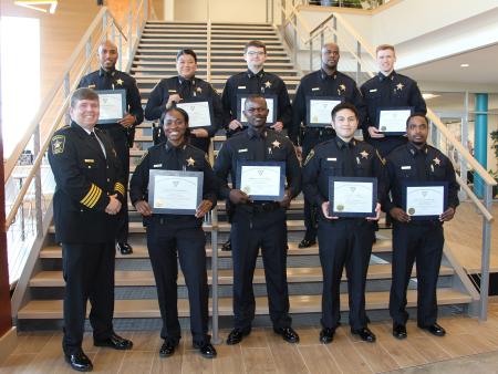 Sheriff in formal uniform standing with nine deputies in dark blue uniforms and holding certificates