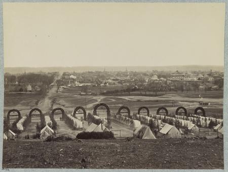 Photo taken from Shuter's Hill, the site of the George Washington Masonic National Memorial, looking east. Alexandria is visible in the background. The foreground shows lines of army tents with archways marking the roads between them. 