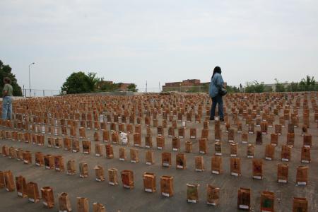 A person walks through a paved lot filled with paper bag luminaries.