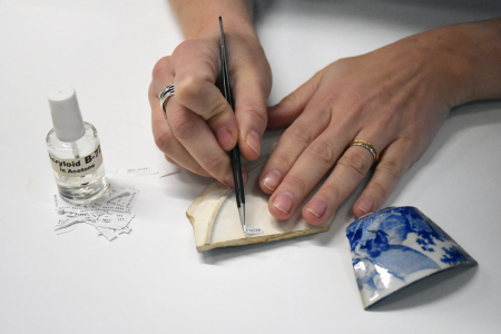 An archaeologist uses tweezers and a removeable glue to add small paper labels to the base of a ceramic artifact