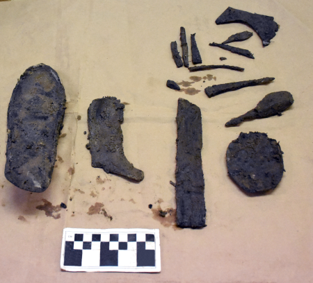 Pieces of leather shoes are laid out on brown paper to be photographed with a scale.