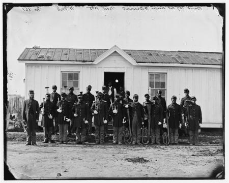 USCT soldiers pose with brass instruments outside of a one-story frame building