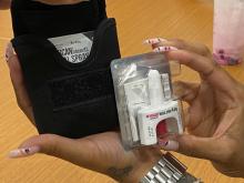 hands holding Narcan nasal spray and a black pouch