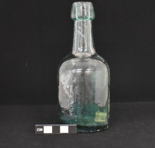 Glass bottle photographed on a black background with a scale for size.