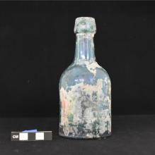 Glass bottle photographed on a black background with a scale for size.