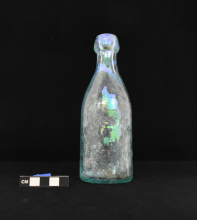 Glass bottle photographed on a black background with a scale for size.